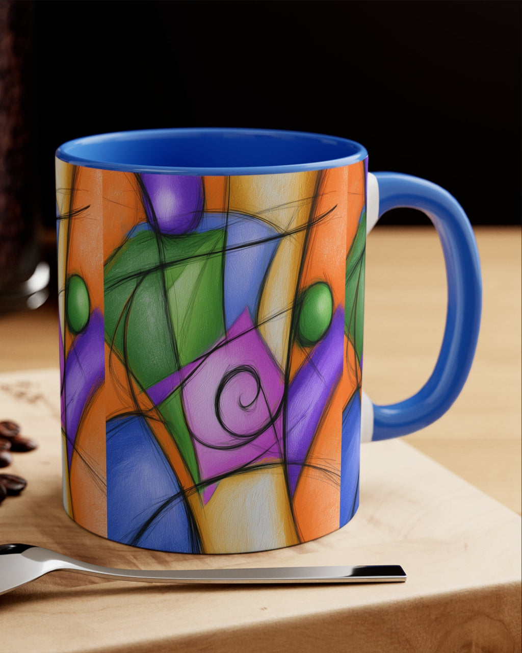 A ceramic coffee mug with a vibrant, multicolored abstract stained-glass style print, featuring a bright blue handle and interior. The mug is styled on a wooden board next to a spoon, coffee beans, and a macaron, with a blurred coffee bean jar in the background.
